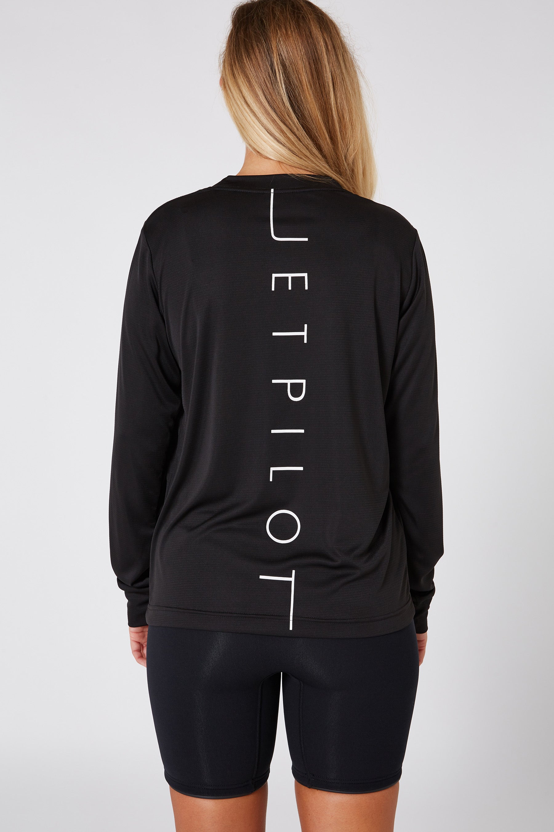 Person wearing a black long-sleeve top with 'JETPILOT' branding on the back against a white background
